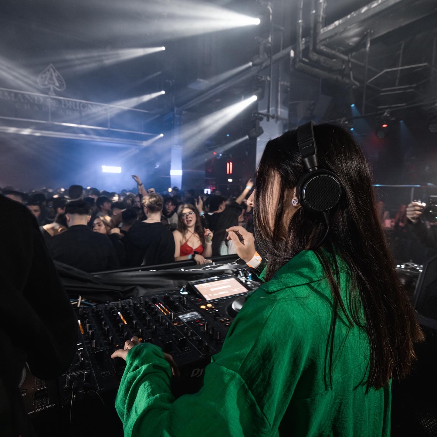 DJ in a green shirt performing as the crowd dances with colorful lights and smoke.