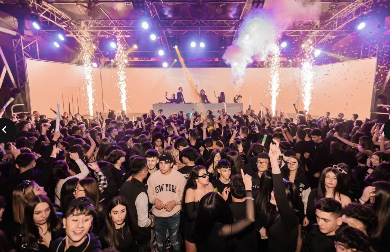 Crowd enjoying a concert with a DJ on stage, sparks and lights enhancing the vibe.