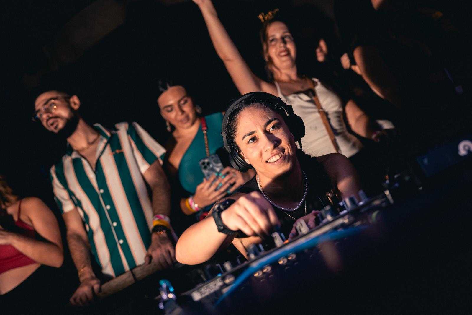 DJ performing at a lively club event with colorful lights and dancing crowd.