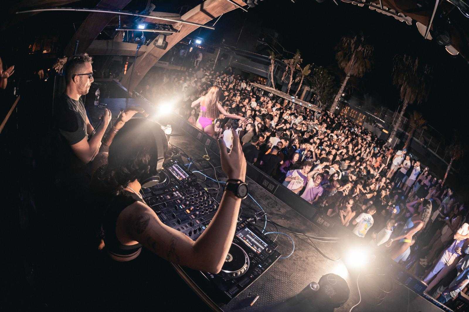 Outdoor concert DJ with a large, energetic crowd, palm trees in the background.