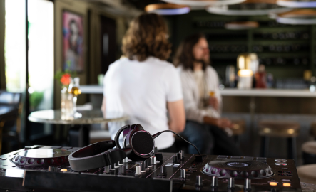 DJ setup with headphones, people talking at a modern bar in the background.